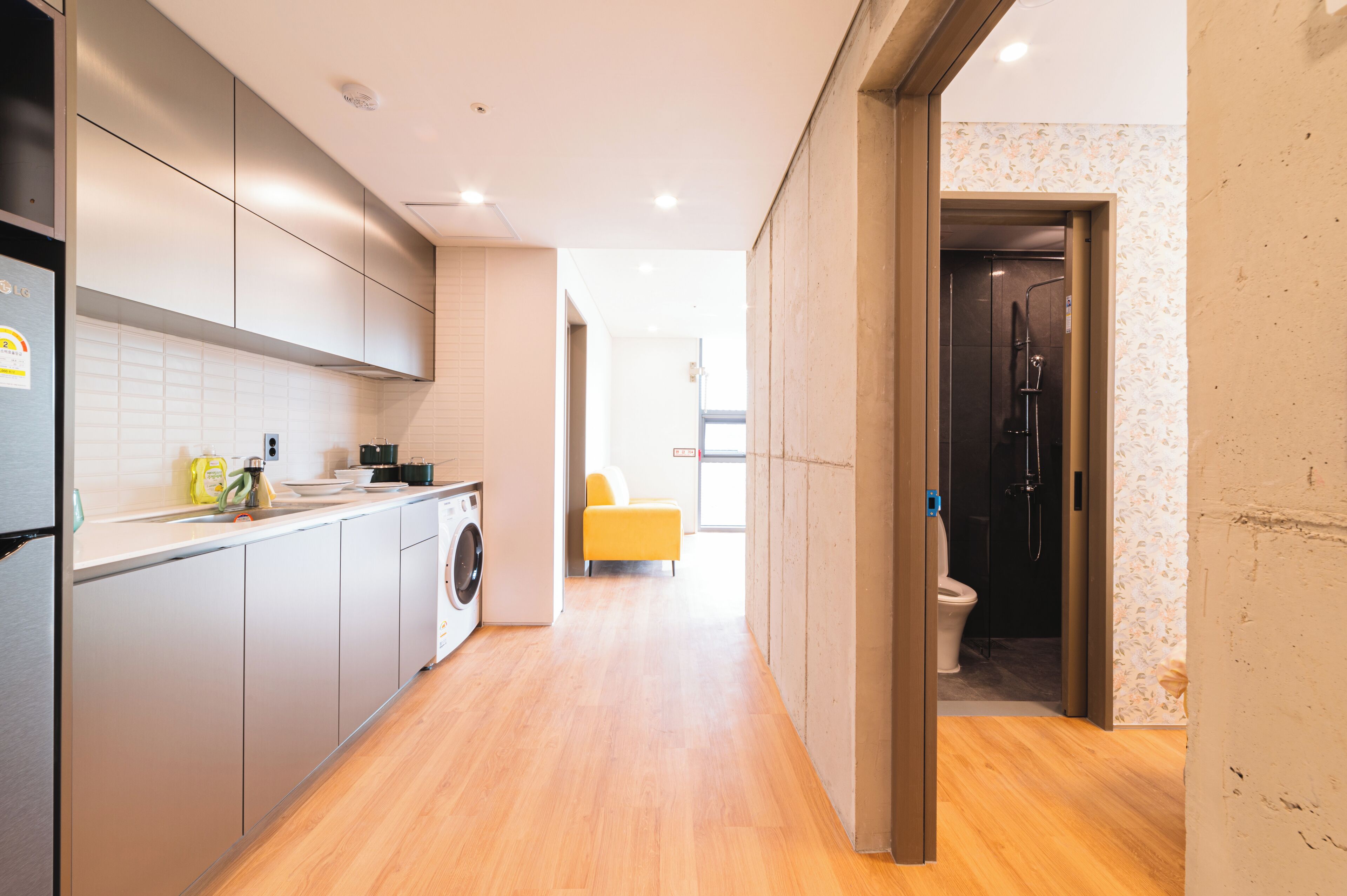 A modern kitchen with a washing machine, a yellow sofa in the living area, and a shower in the bathroom.