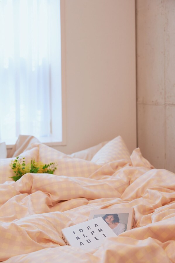 A bed with a checkered blanket, a small plant, and a book titled "IDEA ALBERT" on it.