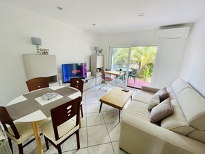 Uma sala de estar moderna com área de jantar, sofá, televisão e varanda com vista para o verde.