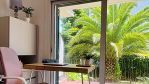 Una habitación con escritorio, silla y vistas a un balcón con palmeras.