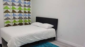 A bedroom with a bed, a blue rug, and a geometric-patterned curtain.