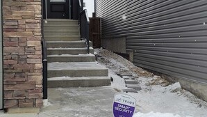 A residential building with a stone facade, a metal garage door, and a snow-covered entrance. - Charming 2-bedroom basement in superb Edmonton with WiFi near WEM (Edmonton)