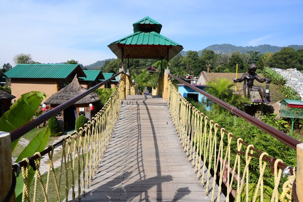 A wooden bridge with rope railings leading to a building with a green roof.