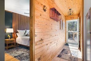 Een houten interieur met een bed, nachtkastje en uitzicht door een glazen deur op een terras.