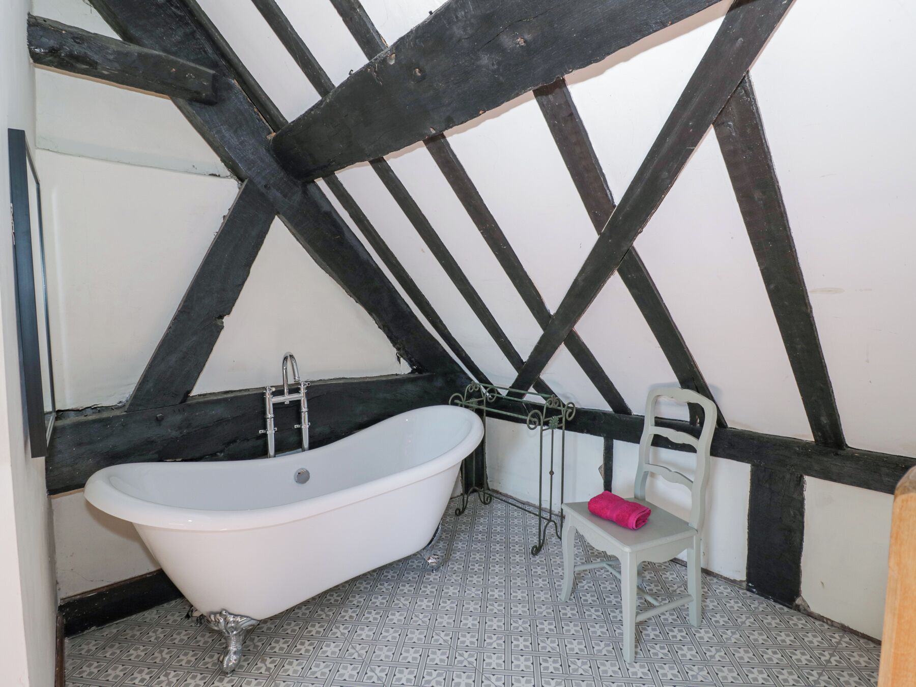 A bathroom with a freestanding bathtub, a white chair, and a tiled floor.