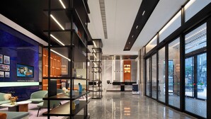 Un moderno vestíbulo de hotel con un mostrador de recepción, zona de estar y ventanas amplias con vistas a la ciudad.