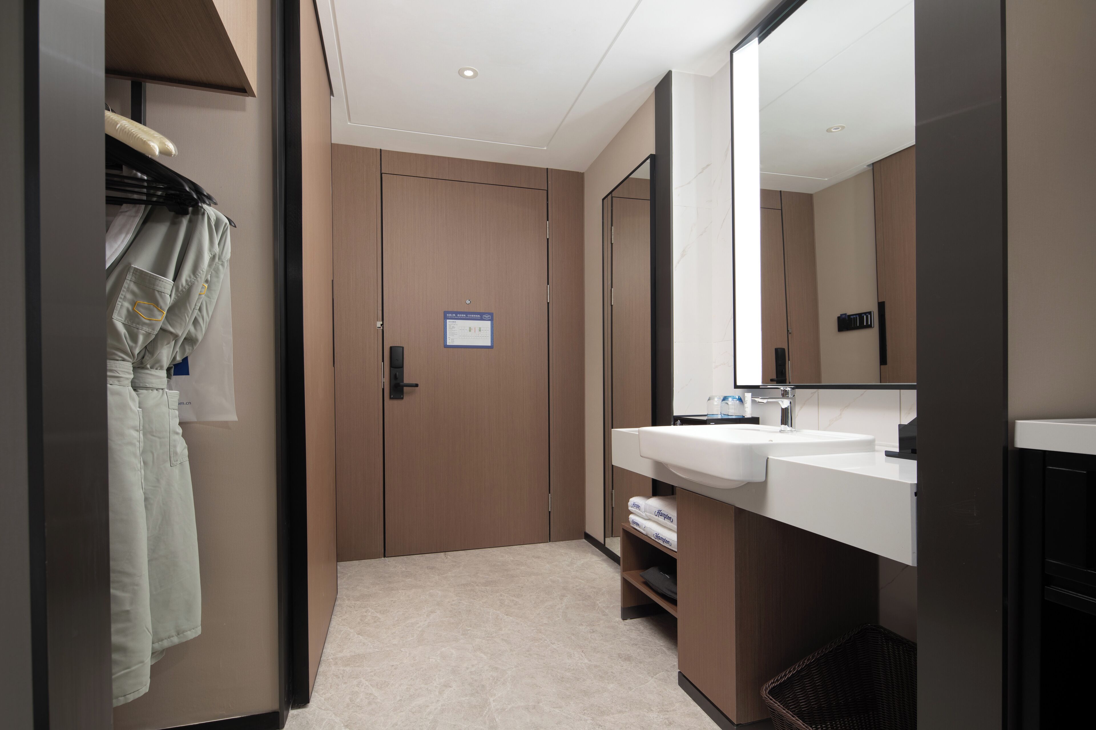 Un baño moderno con puerta de madera, un espejo grande y un lavamanos blanco.