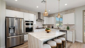 Une cuisine moderne dotée d’appareils électroménagers en acier inoxydable, d’un îlot en marbre et de luminaires suspendus.