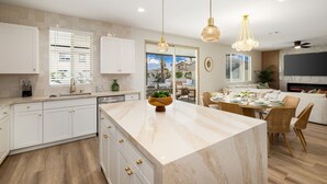 Une cuisine moderne avec des meubles blancs, un îlot en marbre et des luminaires suspendus.