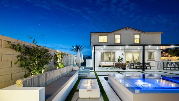 Une terrasse extérieure moderne, dotée d’une piscine, de coins salon et d’une maison bien éclairée en arrière-plan.