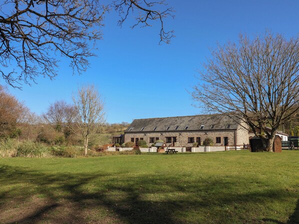 A stone building with multiple windows and a sloped roof, surrounded by a grassy area and trees. - Colombo Cottage (Lyme Regis)