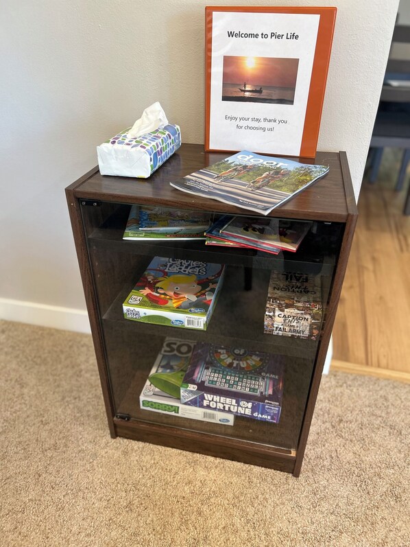 A small wooden side table with a glass display case containing board games and magazines. A welcome sign with a sunset photo is on top. - Little Sturgeon - 5 min to boat launch! (Sturgeon Bay)