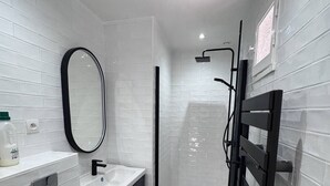Een moderne badkamer met witte metro tegels, een wit toilet, een wastafel met donkere kast, een spiegel en een douche met glazen deur.