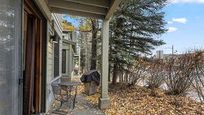 Une véranda abritée avec une table et des chaises, un barbecue et une porte donnant accès à un bâtiment.