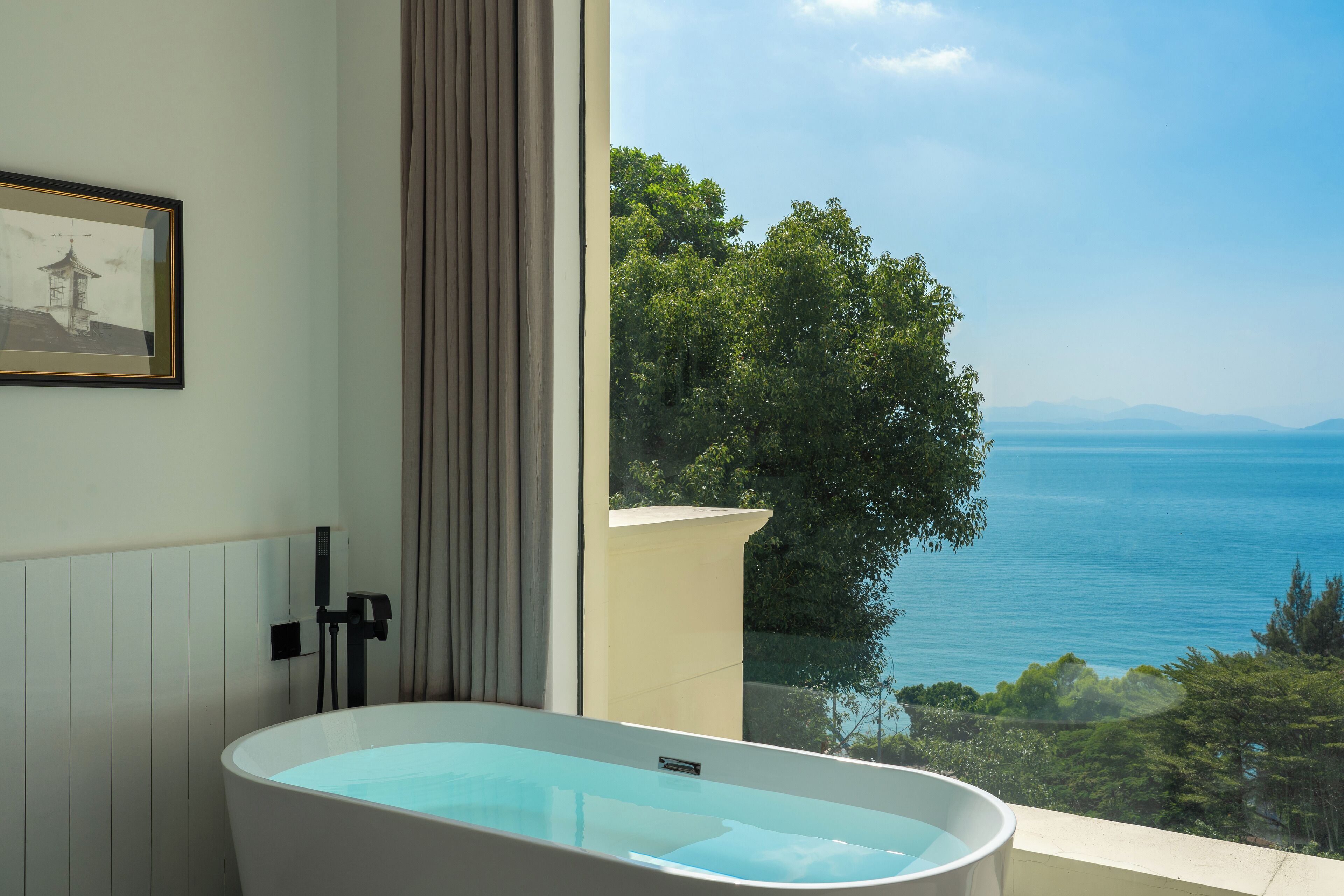 Un baño moderno con bañera, un cuadro en la pared y vistas al mar.