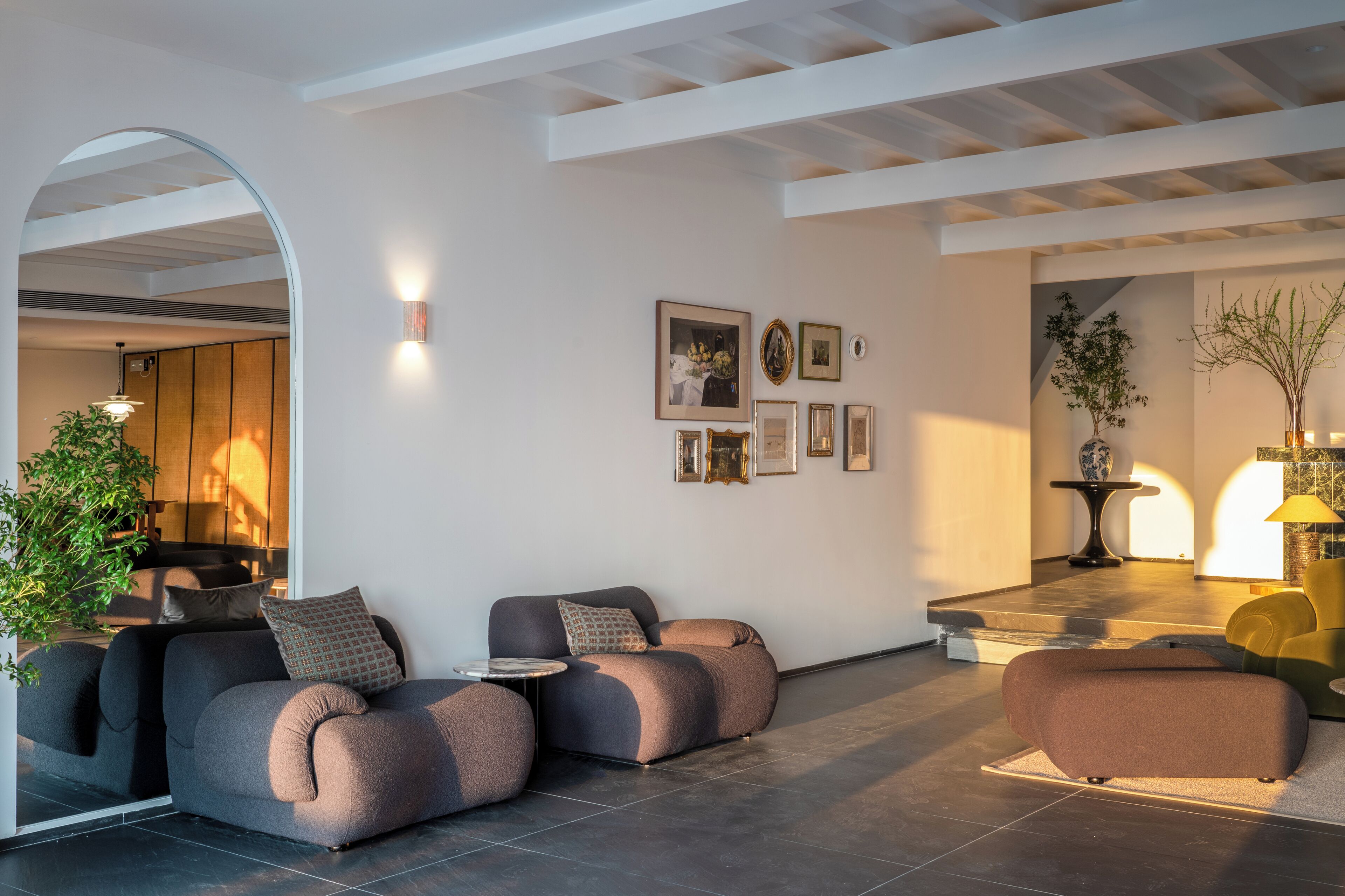 Ein modernes Wohnzimmer mit einer Sofagarnitur, einem Couchtisch und einem kleinen Tisch mit einer Lampe. An der Wand hängen gerahmte Bilder und in der Ecke steht eine Pflanze.