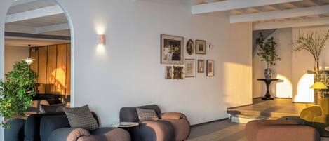 Ein modernes Wohnzimmer mit einer Sofagarnitur, einem Couchtisch und einem kleinen Tisch mit einer Lampe. An der Wand hängen gerahmte Bilder und in der Ecke steht eine Pflanze.