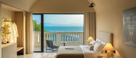 Habitación de hotel con cama, sofá, una mesita con frutero, balcón con vista al mar y un cuadro en la pared.