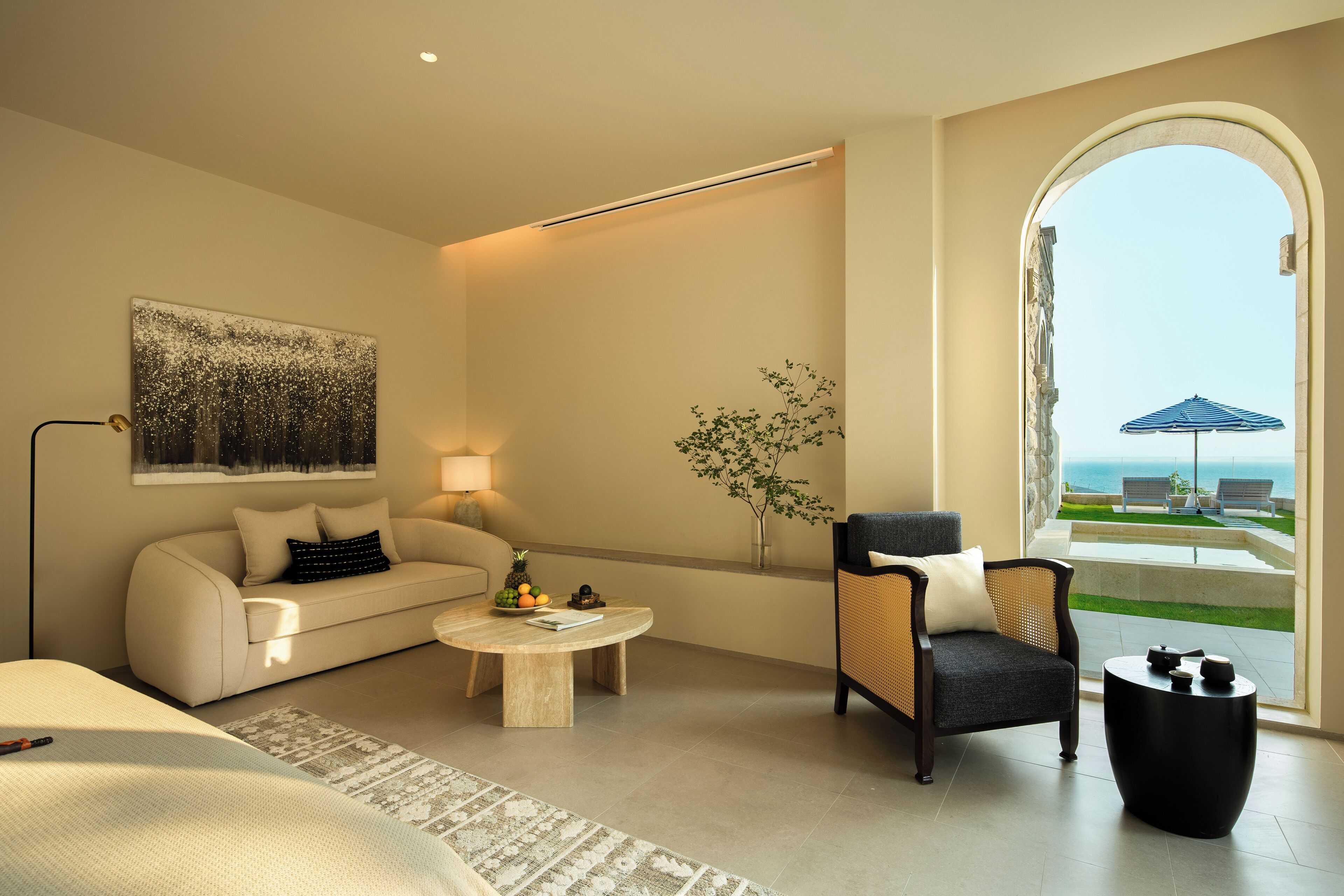 Una habitación de hotel moderna con sofá, sillón, una mesita de café y un amplio ventanal con vista al mar.