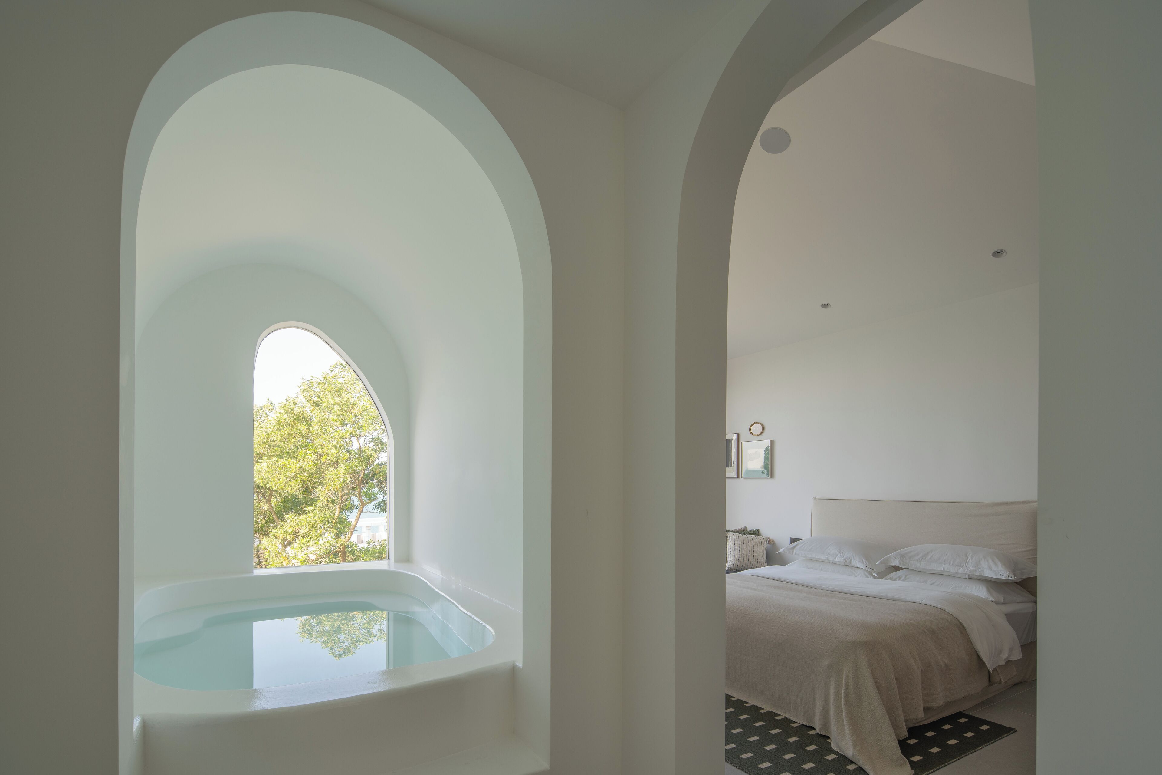 Un dormitorio con un ventanal grande de arco, una cama y una bañera.