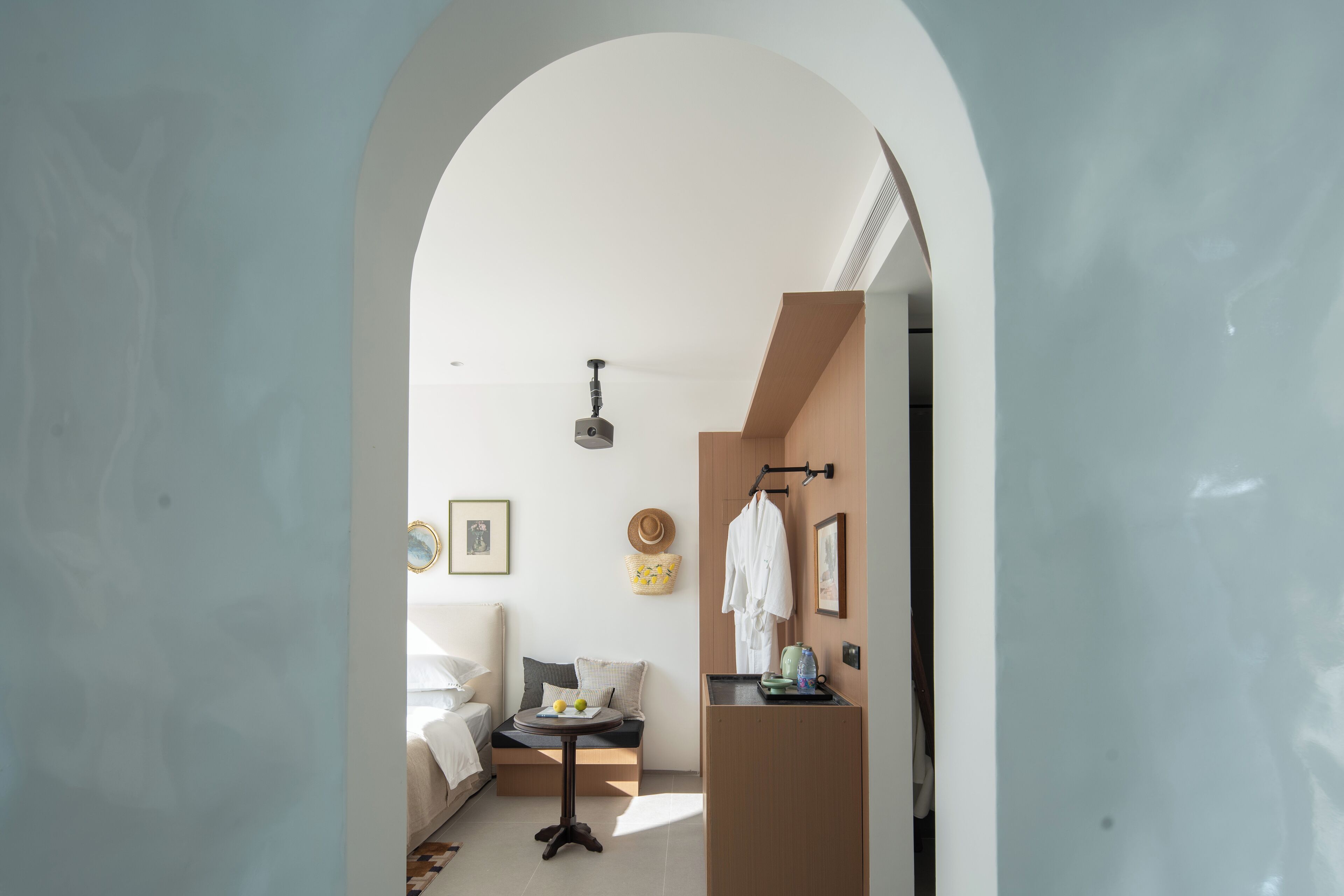 A modern hotel room with a minimalist design, featuring a bed, a small seating area, and a kitchenette.