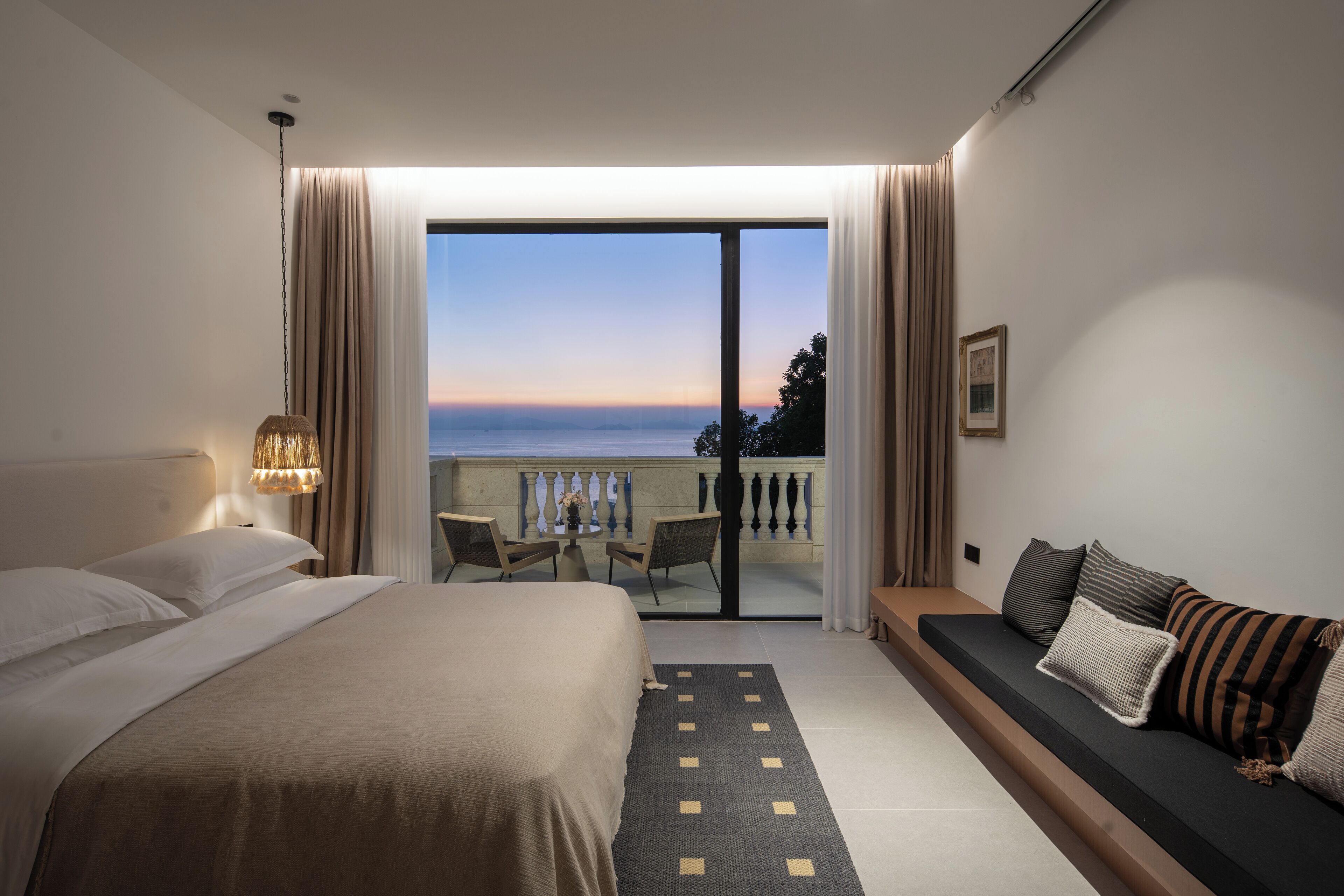 Habitación de hotel con una cama grande, un sofá, un balcón con vistas al mar y un comedor con sillas y una mesa.
