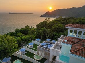 Una villa lujosa con piscina, mobiliario exterior y vista al mar al atardecer.