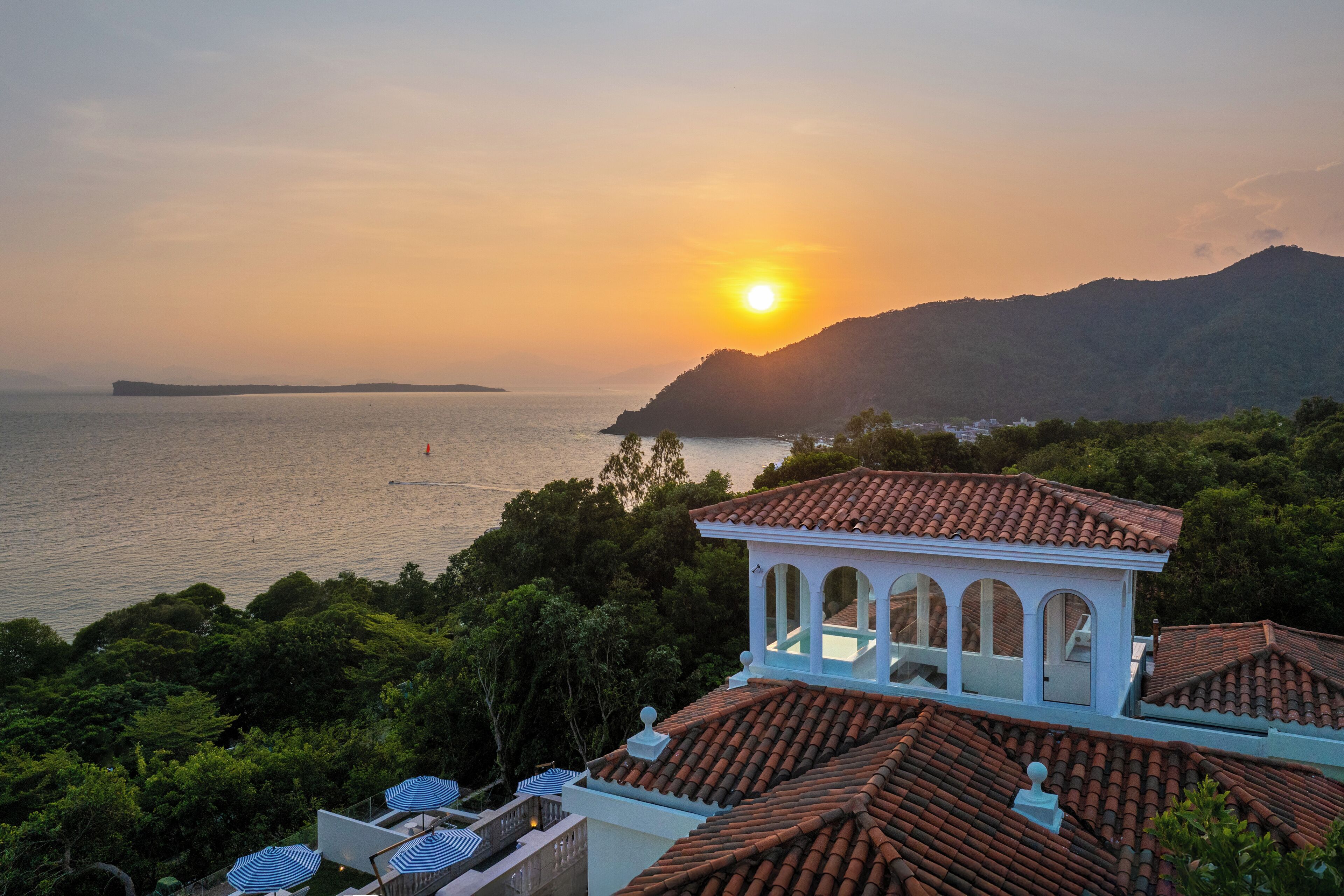 A coastal villa with a terrace overlooking the sea, a swimming pool, and lush greenery.