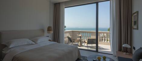 A hotel room with a large bed, a small round table with two lemons, a sofa, and a balcony with a view of the sea.