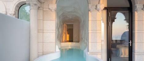 A spa area with a large, clear water feature in the center, surrounded by stone architecture and a glass door entrance.