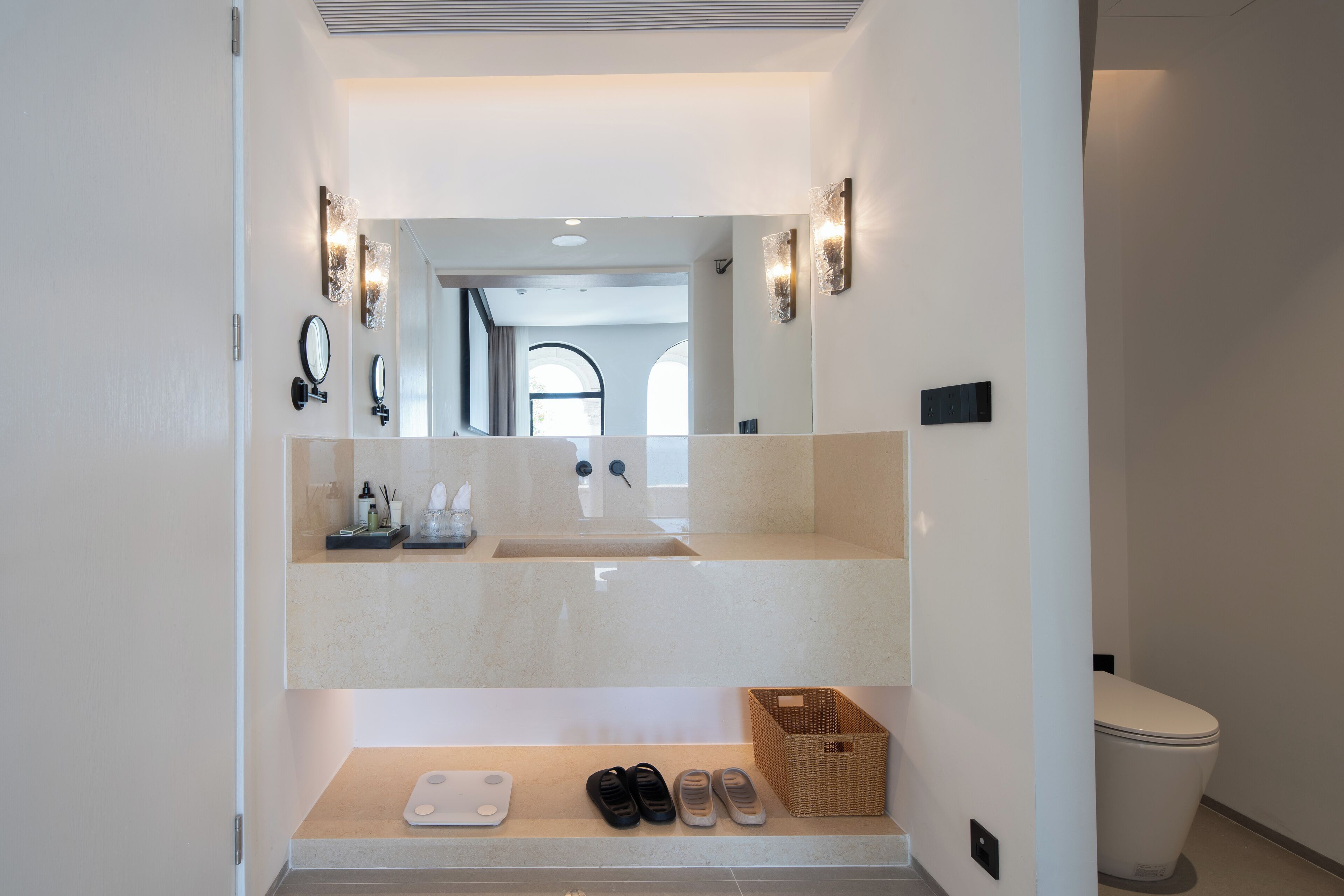 A modern bathroom with a large mirror, two wall-mounted lights, a sink, and a toilet.