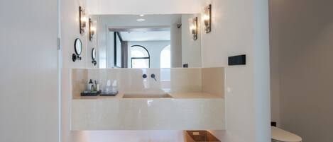 A modern bathroom with a large mirror, two wall-mounted lights, a sink, and a toilet.