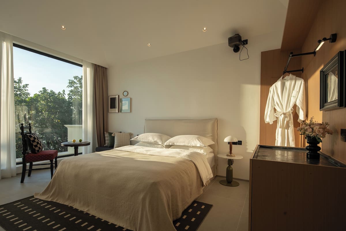 Moderni hotellihuone, jossa on suuri sänky, yöpöytä, tuoli ja näkymä ulos.