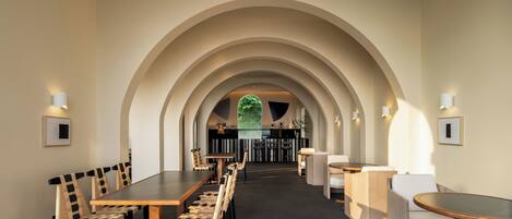 A modern dining area with a long table and chairs, an arched ceiling, and a view of a bar area in the background.