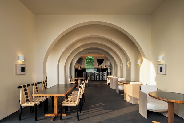 A modern dining area with a long table and chairs, an arched ceiling, and a view of a bar area in the background.