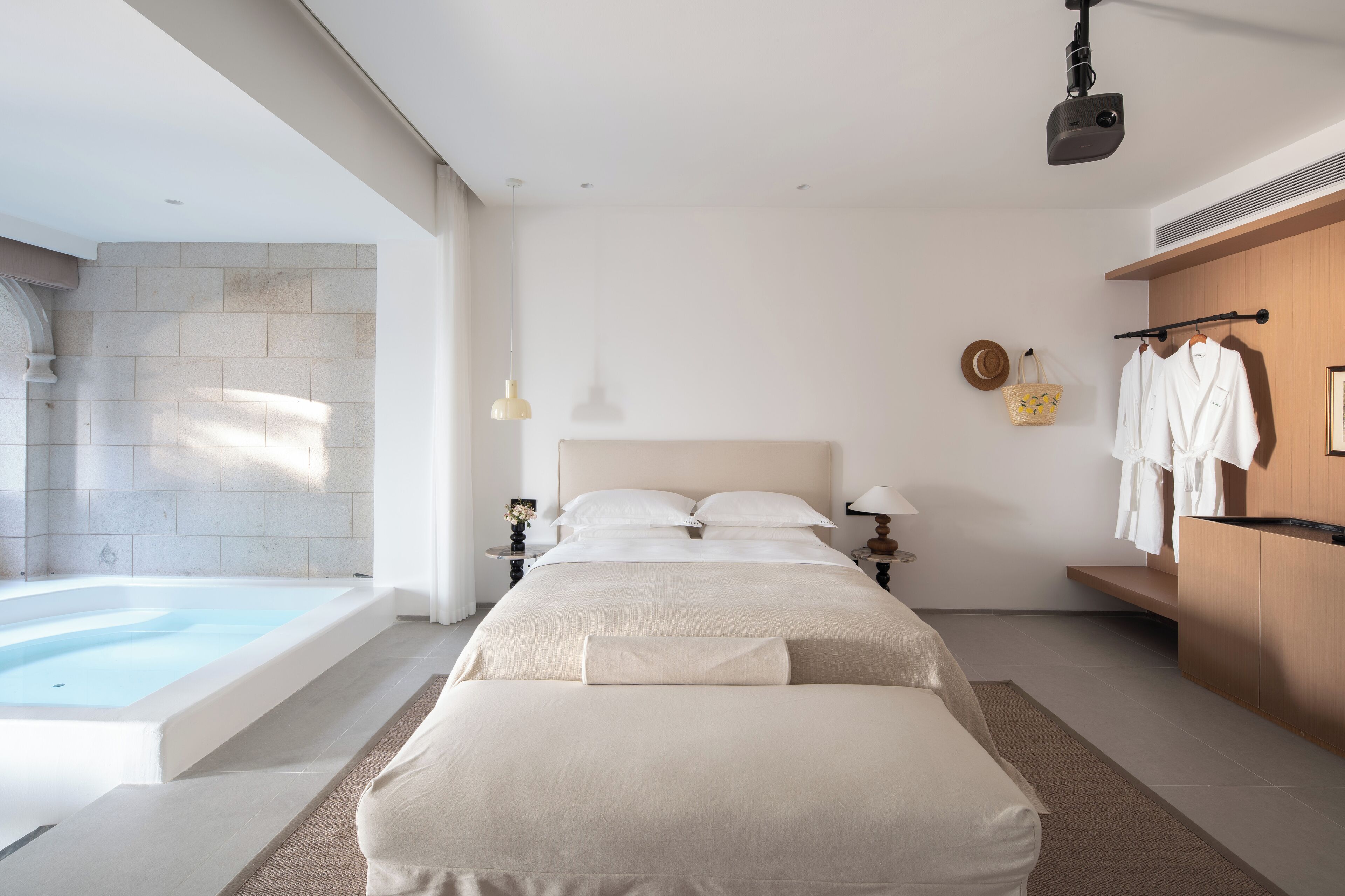 A modern bedroom with a large bed, a bathtub, and a wooden shelf with towels.
