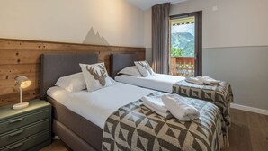 Ein Hotelzimmer mit zwei Betten, Holz Kopfteilen, Blick auf Berge und einem Nachttisch mit Lampe.