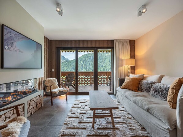 A living room with a fireplace, sofa, and a view of a mountainous landscape through large sliding doors.