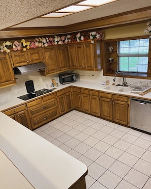 A kitchen with wooden cabinets, a microwave, a sink, and a window with blinds. - Homestayy (Dallas)