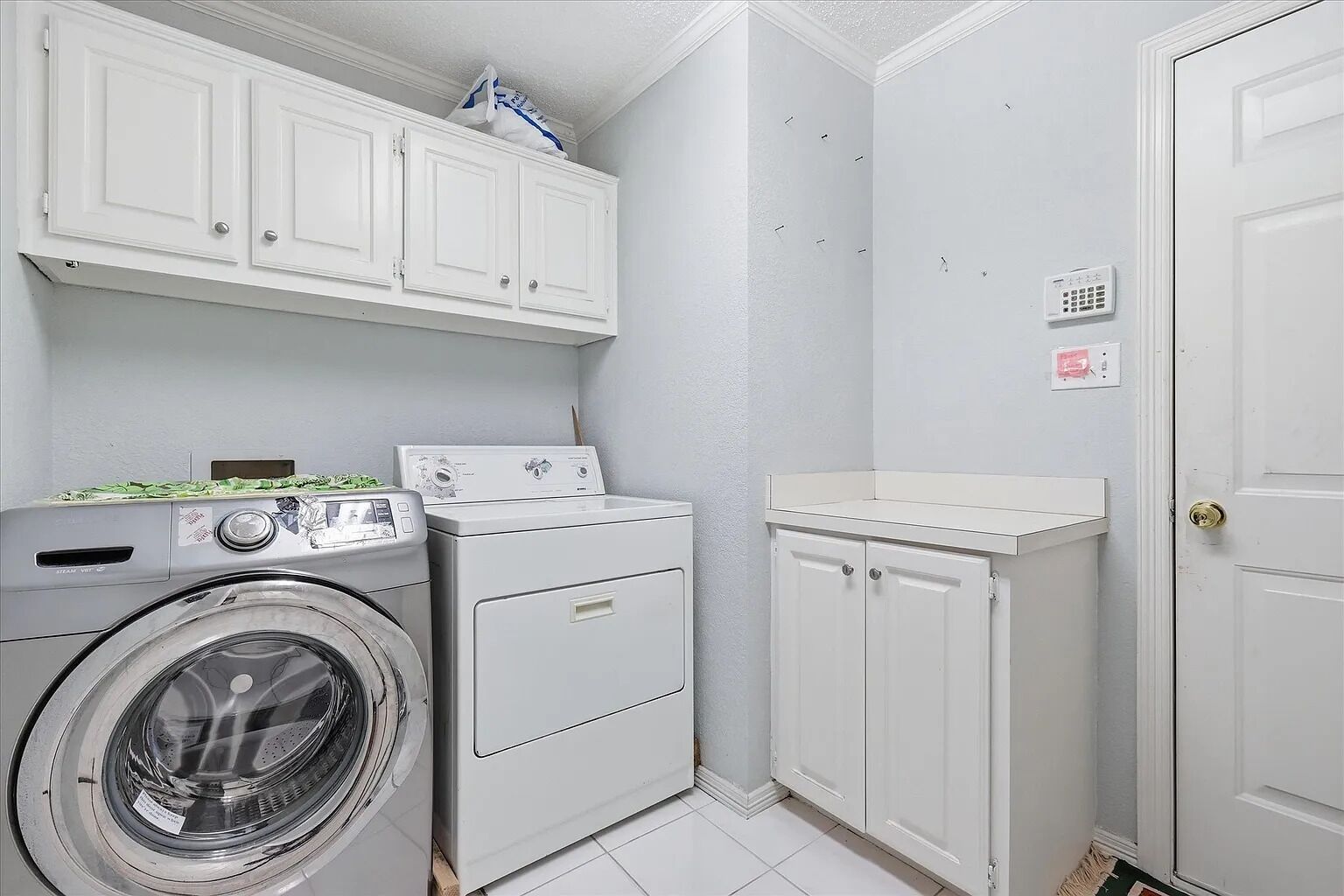 A laundry room with a front-loading washer, a stacked dryer, and a set of white cabinets.
