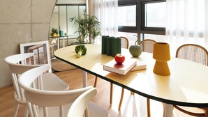 Et moderne spiseområde med et rundt bord, hvide stole, en potteplante og et vindue med lette gardiner.