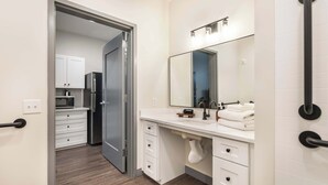 Un baño moderno con tocador blanco, un espejo grande y un perchero para toallas.