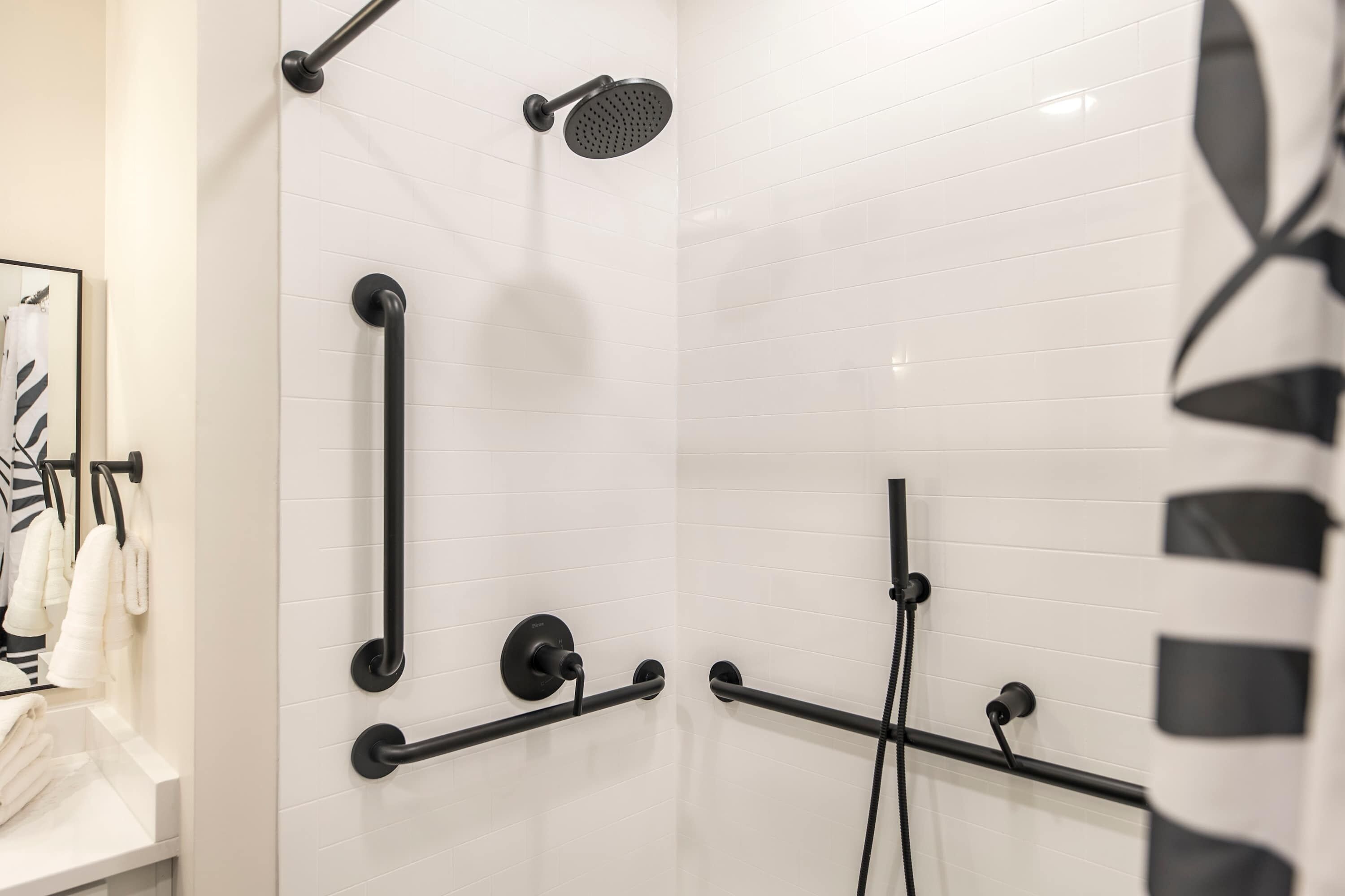 A modern bathroom with white tiled walls, a black showerhead, and a handrail.