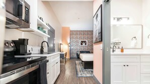 Een compacte keuken met moderne apparaten, een klein eethoekje en een slaapkamer met een grote spiegel en een bed.
