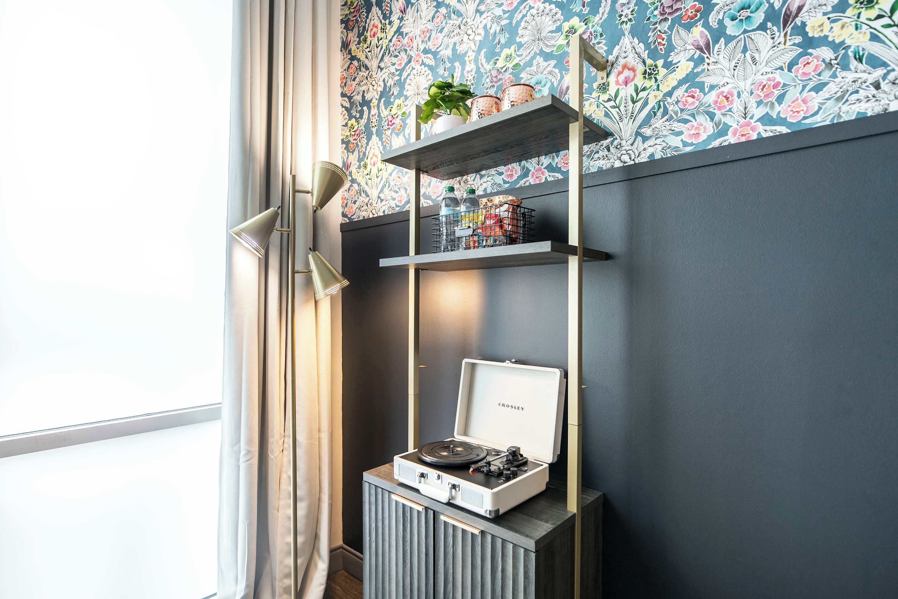 Ett rum med en gammal radio från Crosley placerad på ett träskåp, en hylla i metall med dekorativa föremål och en blommig tapet.
