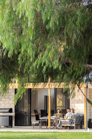 An outdoor patio with a grill, seating, and a glass door leading to a room.