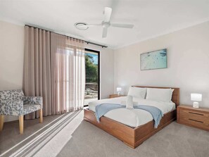 A bedroom with a bed, a chair, a nightstand, a ceiling fan, and a window with curtains.