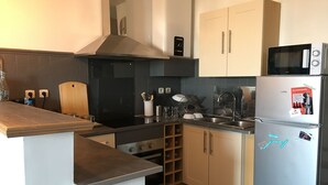 Una cocina moderna con estufa integrada, microondas y electrodomésticos de acero inoxidable. Cuenta con armarios de madera y una salpicadera negra.