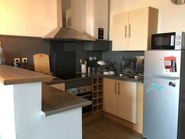 A modern kitchen with a built-in stove, microwave, and stainless steel appliances. There are wooden cabinets and a black backsplash. - Lovely T2 apartment - 40m2 - Sea view and port du môle. (Sète)