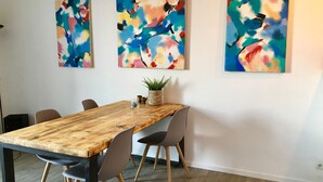 Un comedor con una mesa de madera, cuatro sillas y tres cuadros abstractos en la pared.